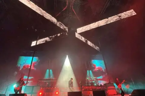 Deftones koncert Polska. Wokalista na scenie, gitarzyści grają, a za nimi ekrany z wizualizacjami.