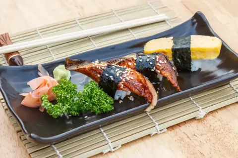 Wyśmienite unagi sushi z sezamem, podane z wasabi, imbirem i natką pietruszki na czarnej tacce.