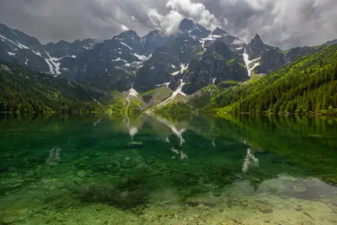 Morskie Oko z rowerem w tle, odbijające się w krystalicznie czystej wodzie. Majestatyczne góry i gęsty las tworzą malowniczy krajobraz.