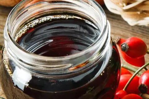Słoik z ciemnym syropem z dzikiej róży, obok świeże owoce. Idealny przepis na domowy syrop z dzikiej róży.