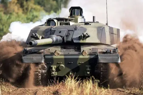 Challenger 2, potężny czołg, pędzi przez teren, wzbijając tumany kurzu i dymu.
