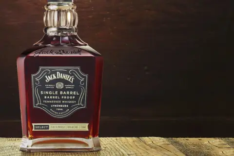Butelka Jack Daniel's Single Barrel Tennessee Whiskey, z bogatym, bursztynowym kolorem, stoi na drewnianym blacie.