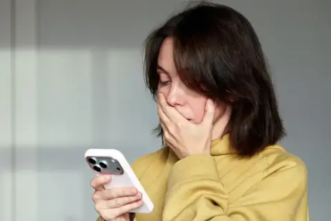 Zaskoczona kobieta zasłania usta dłonią, patrząc na telefon. Czyżby zobaczyła coś niepokojącego, a może to numer 883 co to za numer?