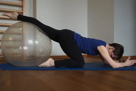 Kobieta na macie ćwiczy z piłką, rozciągając nogę. Widać, co daje stretching: lepsza gibkość i relaks.