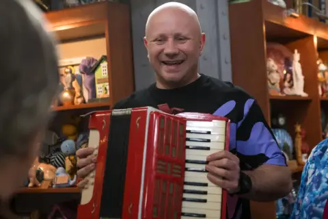 Mariusz z lombardu, grając na akordeonie, wygląda na szczęśliwego. Nie wiadomo, ile lat ma Mariusz z lombardu.