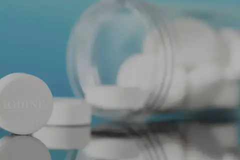 Pastillas de yodo blancas, una en primer plano con la palabra "IODINE" grabada, y un frasco volcado con más pastillas.