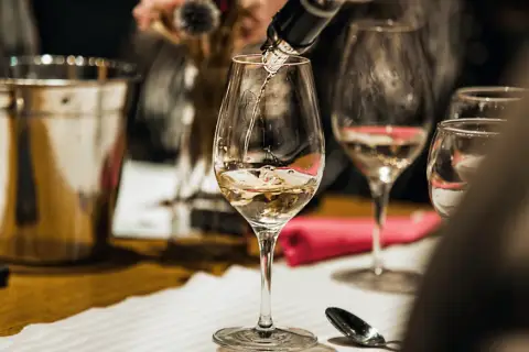 Jak zaplanować degustację wina w domu dla grupy znajomych? Nalewanie białego wina do kieliszków, przygotowanie stołu.