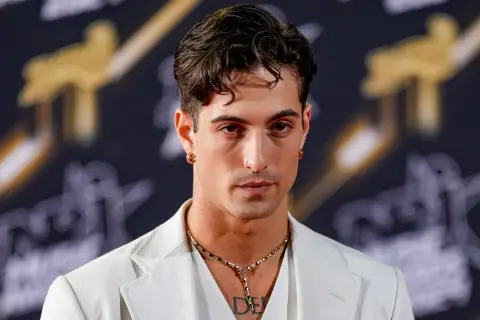 Damiano David w białej marynarce, z naszyjnikiem i kolczykami, gotowy na koncert.