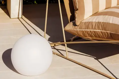 Una lámpara suelo esférica ilumina la terraza junto a un sillón a rayas.