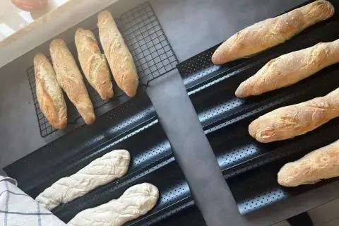 Gotowe do pieczenia bagietki po francusku, świeżo wyrośnięte ciasto i wypieczone bochenki na ruszcie.