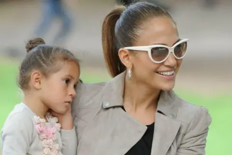 Jennifer Lopez z córką, Emme, w słoneczny dzień. Dziewczynka przytula się do mamy, która uśmiecha się do obiektywu.