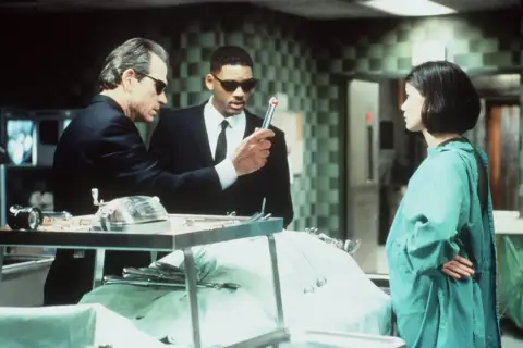 Faceci w czerni obsada: Tommy Lee Jones i Will Smith badają tajemniczy obiekt, podczas gdy Lara Flynn Boyle obserwuje.