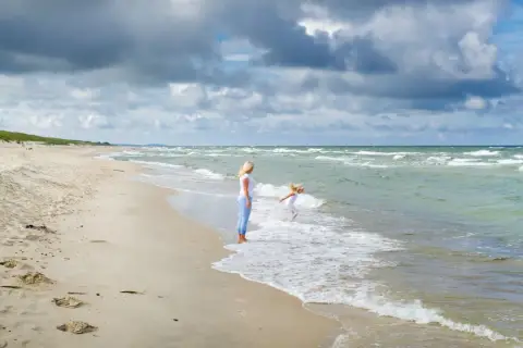 Matka patrzy, jak dziecko bawi się w falach. Czy Szwecja ma dostęp do Morza Północnego? Tak, przez cieśniny Skagerrak i Kattegat.