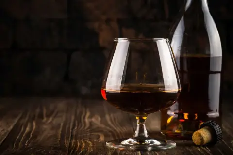 Kieliszek brandy i butelka na drewnianym stole. Idealny moment, by zastanowić się, z czym pić brandy.