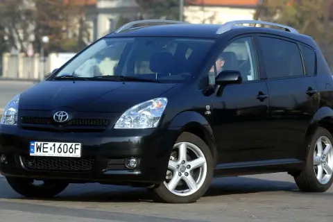 Czarny Toyota Corolla Verso z relingami dachowymi, zaparkowany na ulicy.