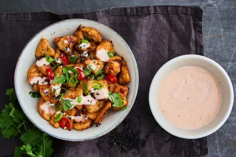 Krispiga kycklingbitar toppade med färska örter, chili och sesamfrön, serverade med en krämig bang bang sås.