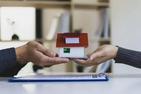 Dwie dłonie przekazują sobie miniaturowy dom. Symbolizuje to automatyczne przyjęcie spadku i przekazanie majątku.