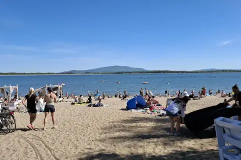 Słoneczny dzień nad jeziorem Mietkowskim. Ludzie odpoczywają na plaży, niektórzy kąpią się w wodzie.