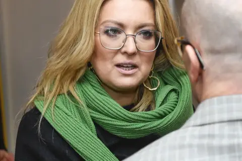 Kinga Burzyńska w zielonym szaliku i okularach rozmawia z mężczyzną.