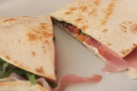 Pyszna piadina romagnola z szynką, pomidorami i rukolą, złożona na pół, gotowa do jedzenia.