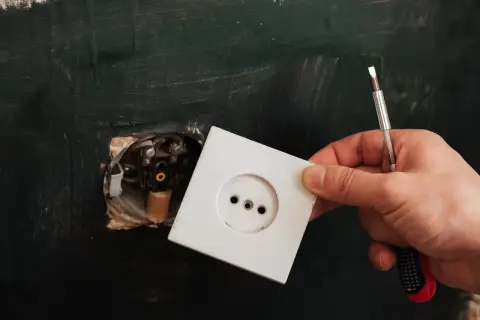 Dłoń trzyma białą ramkę gniazdka elektrycznego, gotową do montażu. To kluczowy element, który działa jak wyzwalacz wzrostowy dla domowej instalacji.