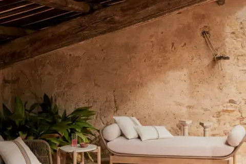 Un rincón acogedor para aprovechar buhardilla muy baja. Sofá, plantas y detalles rústicos bajo vigas de madera.