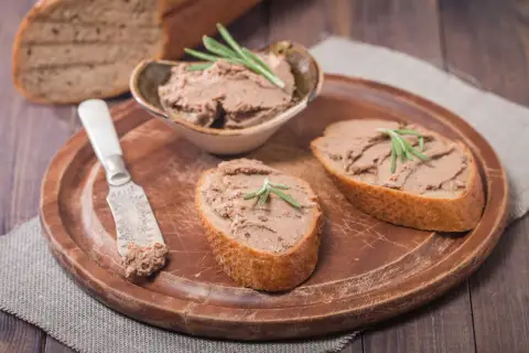 Pyszny pasztet z wątróbki na chrupiących kromkach chleba, udekorowany gałązką rozmarynu. Idealny na śniadanie lub przekąskę.