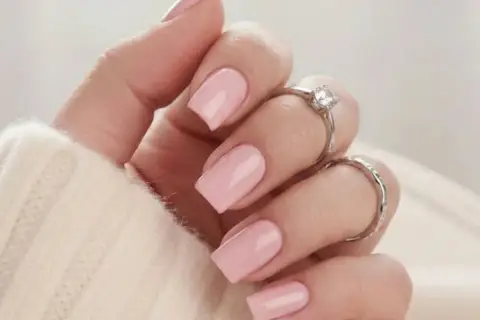 En hand med naglar målade i mjukt nagellack rosa, prydd med två silverringar.