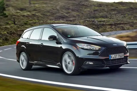 Czarny Ford Focus 3 kombi na zakręcie malowniczej drogi.