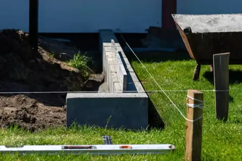 Budowa fundamentu pod ogrodzenie. Betonowe bloczki tworzą solidną podstawę, a poziomica i sznurek pomagają w precyzyjnym ułożeniu.