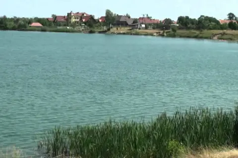 Spalona jezioro z domkami na brzegu. Woda jest turkusowa, a na pierwszym planie rośnie trzcina.