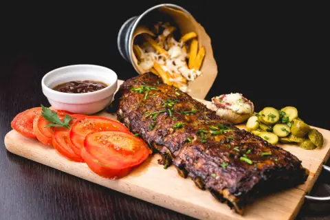 Délicieux ribs de porc, parfaitement cuits, accompagnés de frites, tomates et cornichons. Un festin pour les amateurs de cuisson ribs.