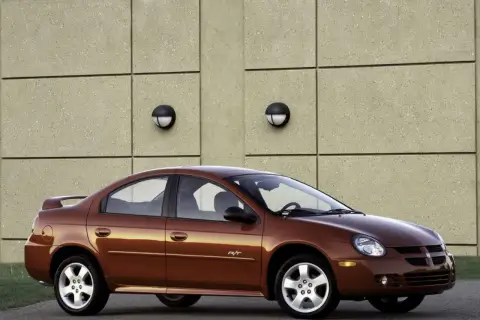 Brązowy Dodge Neon R/T z 2004 roku stoi przed betonową ścianą z dwoma okrągłymi lampami.