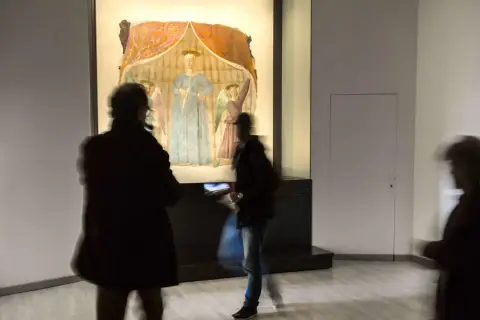 La Madonna del Parto di Piero della Francesca, con visitatori che la ammirano in un museo.