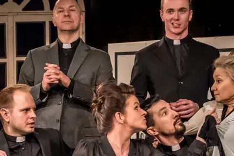 Na scenie Teatru Capitol rozgrywa się intryga. Aktorka w stroju pokojówki trzyma dzbanek, a wokół niej zgromadzeni mężczyźni w sutannach i jeden w stroju lokaja.