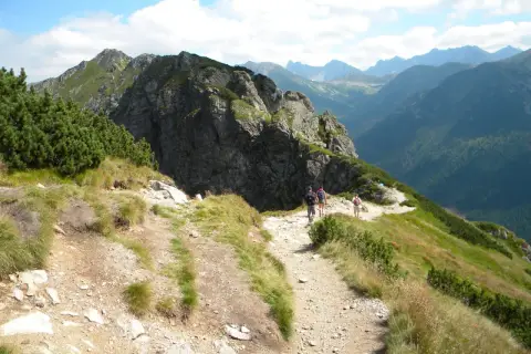 Turyści idą kamienistym szlakiem w Tatrach. Widok na góry i lasy. Idealne tatry szlaki dla średnio zaawansowanych.