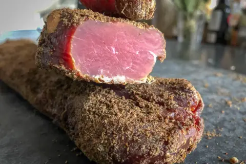 Un morceau de viande séchée, enrobé d'épices, dégage une odeur délicatement boucanée. Sa chair rose vif contraste avec sa croûte brune.