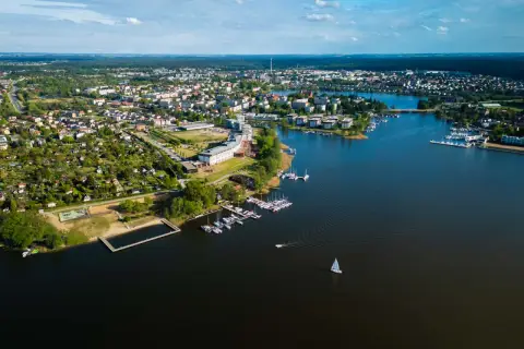 Malownicze miasto nad Jeziorakiem, z mariną pełną żaglówek i łodzi, otoczone zielenią i zabudową mieszkalną.