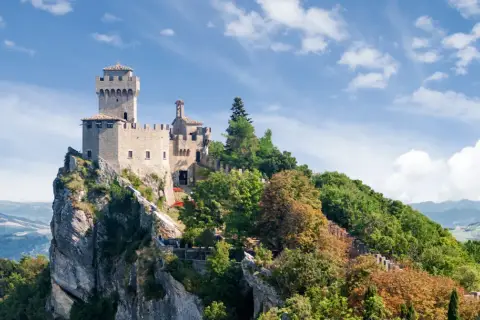 Trzy wieże San Marino na skalistym szczycie, otoczone zielenią. Widok na doliny, gdzie mieszka san marino ludność.