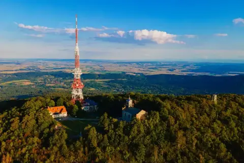 Wieża telekomunikacyjna na szczycie Ślęży, otoczona lasem i budynkami. Widok na rozległą dolinę.