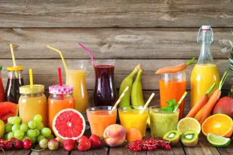 Varietà di bevande colorate e freschi estratti di frutta, con frutta intera e a fette su uno sfondo di legno.
