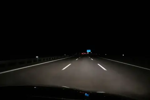 Fahrt über die Autobahn nachts. Scheinwerfer beleuchten die Fahrbahn, weiße Linien weisen den Weg in die Dunkelheit.