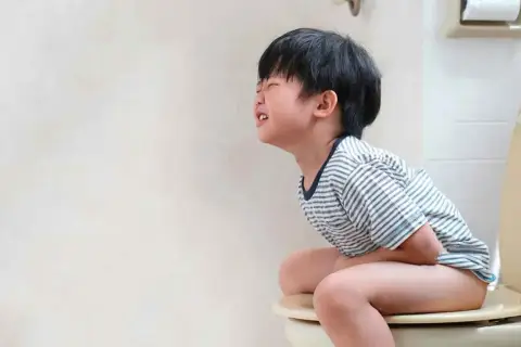 Niño de 5 a 10 años con estreñimiento, sentado en el inodoro con dolor y esfuerzo.