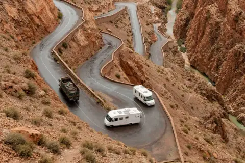 Deux camping-cars naviguent sur une route sinueuse à flanc de montagne au Maroc, traversant un paysage désertique spectaculaire.