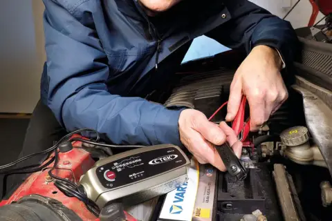 Mężczyzna podłącza prostownik CTEK do akumulatora, by sprawdzić, jak sprawdzić czy prostownik jest dobry.