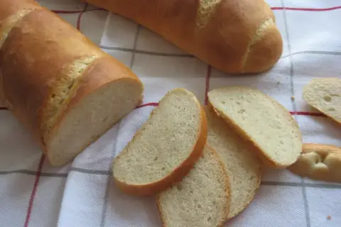 Chleb pszenny na zakwasie, pokrojony w kromki, leży na kratkowanym obrusie. Idealny do śniadania.