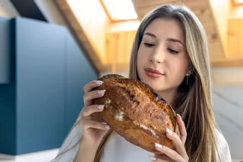 Kobieta trzyma bochenek chleba, zastanawiając się nad jego ładunkiem glikemicznym.