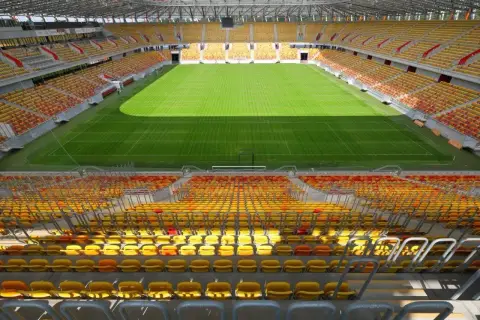 Pusta trybuna stadionu Jagiellonii, z żółtymi i czerwonymi siedzeniami, czeka na kibiców. Pojemność stadionu robi wrażenie.