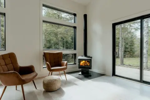 Un poêle à granule appartement, avec deux fauteuils en cuir marron et une vue sur la forêt.