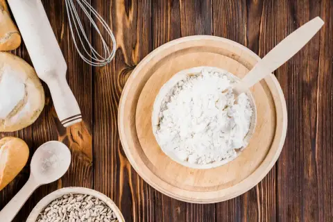 Mąka orkiszowa, podobnie jak pszenna, zawiera gluten. Na zdjęciu widać składniki do pieczenia: mąkę, chleb, ziarna słonecznika, wałek i trzepaczkę.